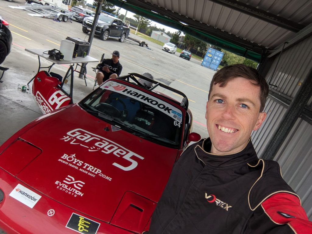 Me smiling in front of Eevees red MX5 in the garages at Ruapuna (Euromarque motorsport park)